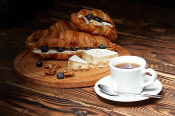 Cup of coffee with croissants, Camembert cheese, blueberries on a wooden background.
