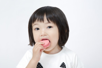 スイーツのマカロンを手に持ち食べている幸せ表情の幼い女の子。幸せ、スイーツ、食欲、楽しい、子供、幼児イメージ