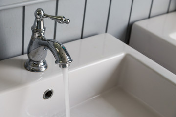 Water running from an open water faucet with white sink