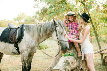 Beautiful young girl with blond hair in a suede jacket with fringe with little sister in a straw...