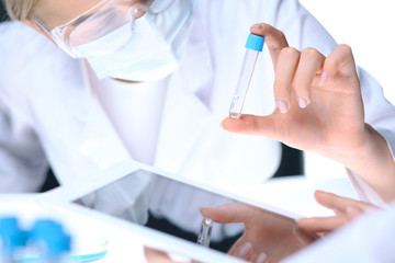 Closeup of scientific research team with clear solution in laboratory. Blonde female chemist holds test tube of glass while her colleague checks results with tablet pc. Blood test, medicine or