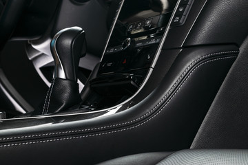 Modern Luxury car inside. Interior of prestige car. Comfortable leather seats with stitching. Black perforated leather cockpit. Steering wheel and dashboard. Automatic gear stick shift. Car detailing