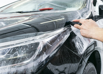 Car wrapping specialist putting vinyl foil or film on car. Protective film. Applying a protective...
