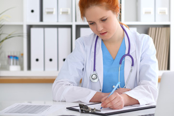 Ginger female doctor filling up medical form on clipboard closeup. Healthcare, insurance and medicine concept