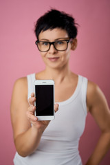 blurred beautiful woman with short hair shows the phone screen on a pink background
