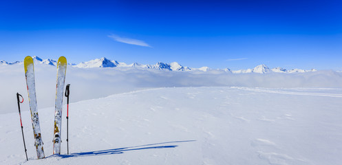 Ski in winter season, mountains and ski touring equipments on the top in sunny day in France, Alps above the clouds.