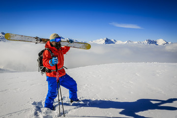 Ski in winter season, mountains and ski touring man on the top in sunny day in France, Alps above the clouds.