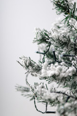 Artificial fir-tree with snow on a white background with an electric garland. Toned photo.
