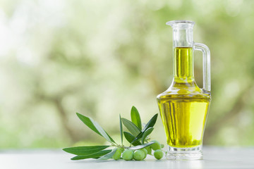 Olive oil in glass bottle outdoor against natural olive trees background.