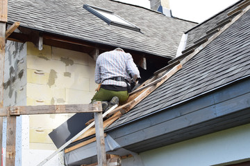 Man working on residential house grey shingles roof construction preparing to insulate building exterior wall with  polyurethane foam sheets. House improvement process and DIY concept.