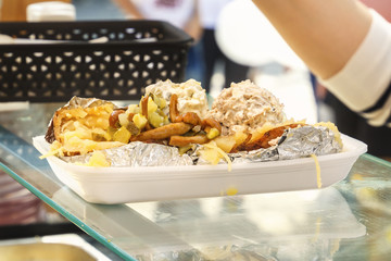 Plate with delicious street food - baked potatoes with sauce, mushrooms and vegetables. Close-up. Copy space