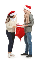 Young woman choosing gift from Christmas bag held by her husband on white background