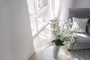 Table with beautiful flowers in vase and cozy armchair for rest near window