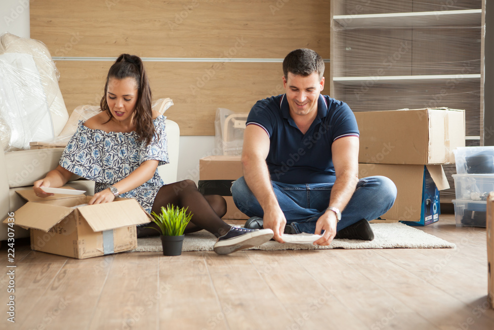 Wall mural happy young couple unpacking boxes in their new flat.couple sitting on the floor.