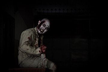 Male zombie sitting and smiles in dark room