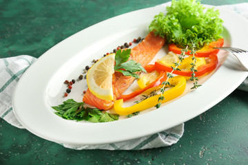 Plate with tasty salmon and vegetable salad on color table