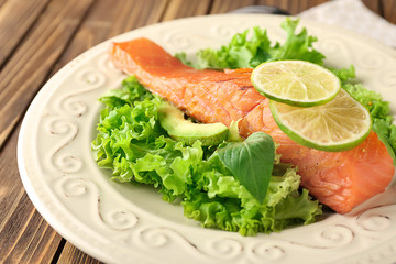 Plate with tasty salmon and fresh salad on wooden table, closeup