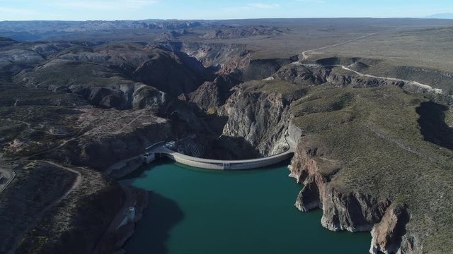 Aerial drone scene of Agua de Toro Dam. Flying very high over lake approaching semi circular dam structure. Mountains and river canyon at background. San Rafael, Mendoza, Argentina