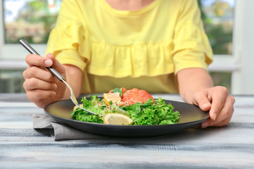 Woman eating fresh salad with salmon at table