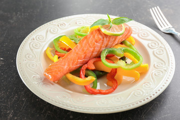 Plate with tasty salmon and fresh peppers on dark table