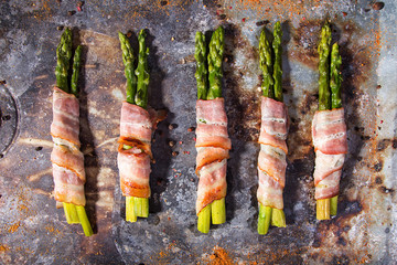 Sticks of green asparagus wrapped with bacon prosciutto ham over on old rusty background. Overhad....