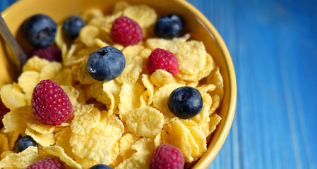 Cornflakes and different Berries - Blueberries and fresh Raspberries, blue wooden background.