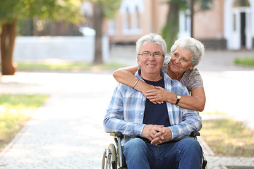Happy senior man in wheelchair and his wife outdoors