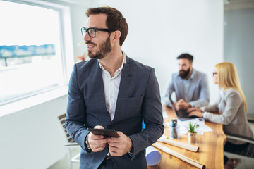 Portrait of young businessman using digital tablet while colleague in background