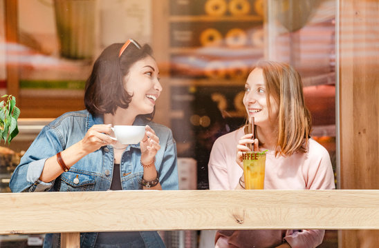 Two happy girls having lunch in a cafe, drinking coffe and talking. Friendship and lifestyle concept