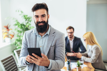 Portrait of young businessman using digital tablet while colleague in background