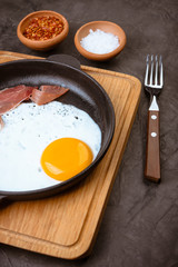 Fried egg in a pan with bacon and  tomatoes  on  black background.