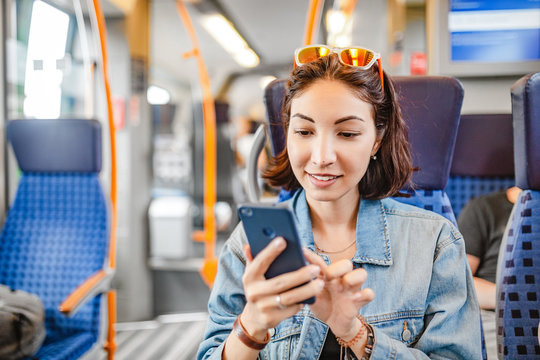 Happy Asian woman using mobile phone app in train