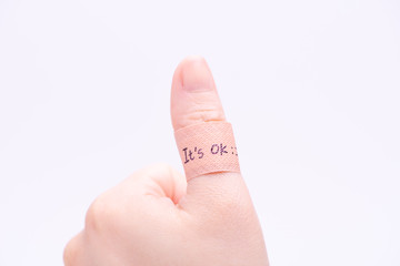 A band aid on thumb up hand with hand writing "It's OK".