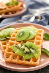 Delicious waffles with kiwi slices on plate