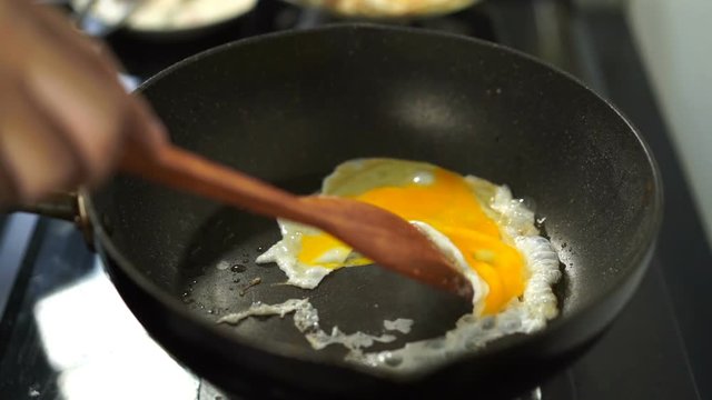 slow-motion of egg frying in pan with wooden turner