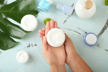 Woman holding jar of natural cream on color background, top view