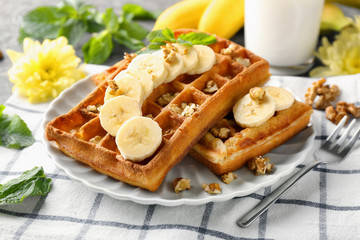 Delicious waffles with banana slices and nuts on plate