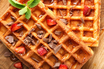 Delicious waffles with strawberries and caramel sauce on wooden table, closeup