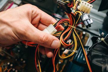 Inside details of the old personal computer. Cooler, motherboard, wires and video card in the dust. Man is holding cables in his hand. Broken PC.