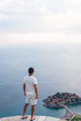 Fototapeta premium back view of man looking at island of Sveti Stefan with hotel resort in Adriatic sea, Budva, Montenegro