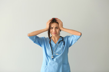 Stressed female nurse on light background