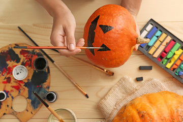 Woman painting pumpkin for Halloween party on wooden table
