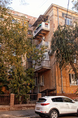 Fragment of an ancient house with balconies with a fence and trees with the parked car.
