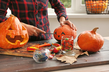 Woman making jack-o-lantern for Halloween party at wooden table