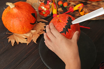 Woman making jack-o-lantern for Halloween party on wooden table, closeup