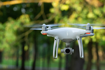 White flying drone with camera on green trees background
