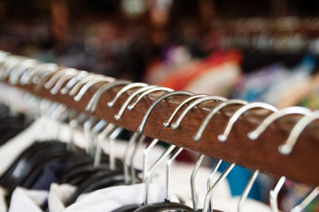 Wooden clothes racks with hangers and with clothes on a blurred background inside shop. - obrazy, fototapety, plakaty