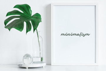 Modern and minimalistic composition of mock up photo frame with green tropical leaf.  Stylish concept of mockup frame. 