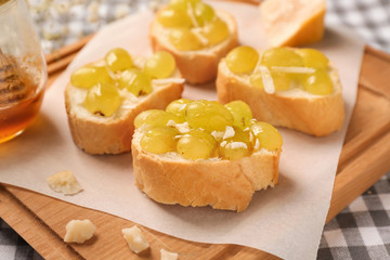 Tasty sandwiches with cheese and grape on wooden board