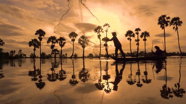 Silhouette of fishermen or fisherman throw fishing nets to catch fish at the pond in the sky morning. Slow motion footage of silhouette fisherman or fisher throwing a fishing net in yellow sky sunrise